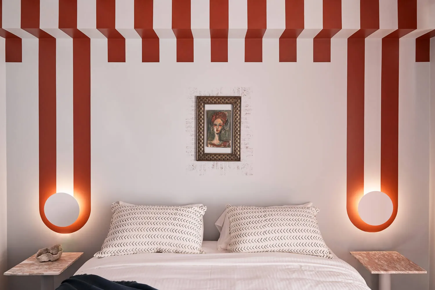 A modern bedroom with a striped ceiling, patterned bedding, and a framed abstract portrait on the wall.