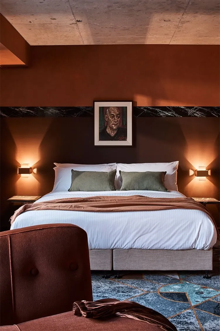 A modern bedroom featuring a bed with green accent pillows and a fabric headboard against a brown and black marble accent wal