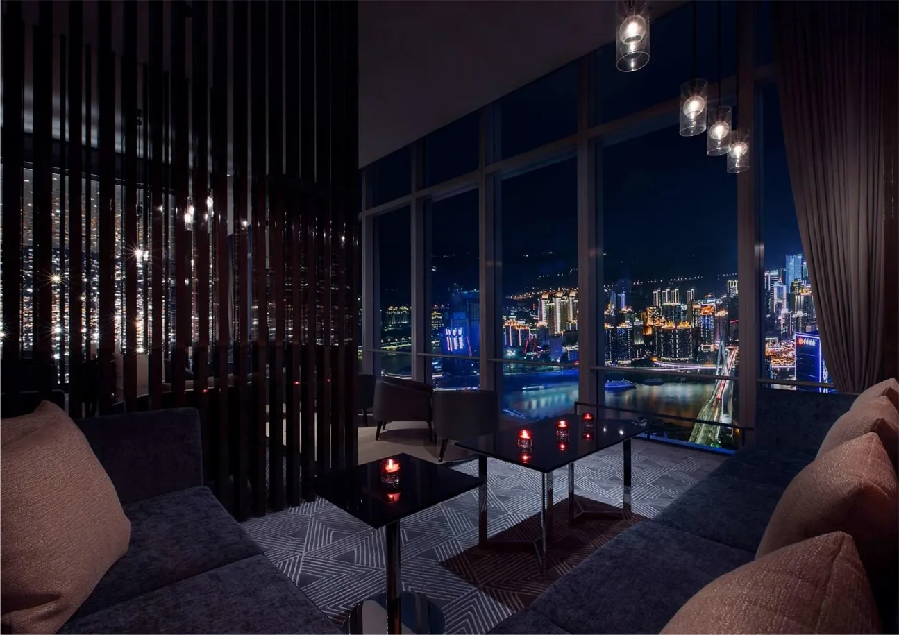 A luxury hotel suite with a city view, featuring modern furniture and large windows.