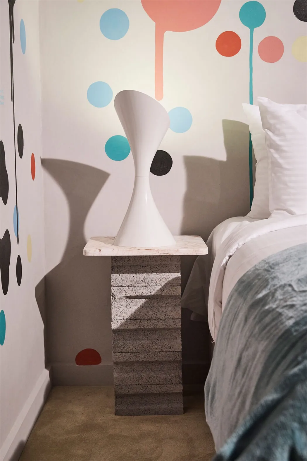 A modern bedroom featuring a stylish bedside table made of concrete and marble, with a unique vase on top.