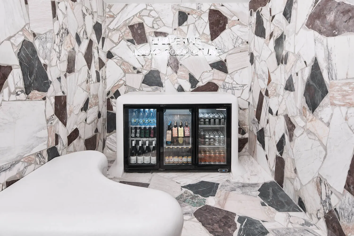 A retail franchise interior with a marble wall and floor, featuring a well-stocked beverage cooler.