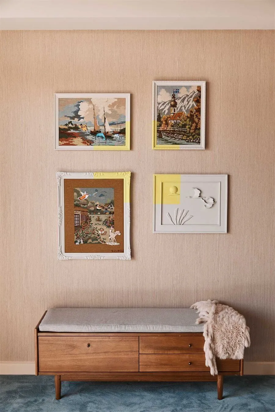Four vintage framed prints on a beige textured wall with a wooden bench below them.