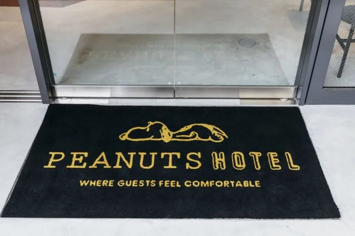 黑色酒店門墊上印有黃色文字「PEANUTS HOTEL WHERE GUESTS FEEL COMFORTABLE」。酒店標誌呈現斜