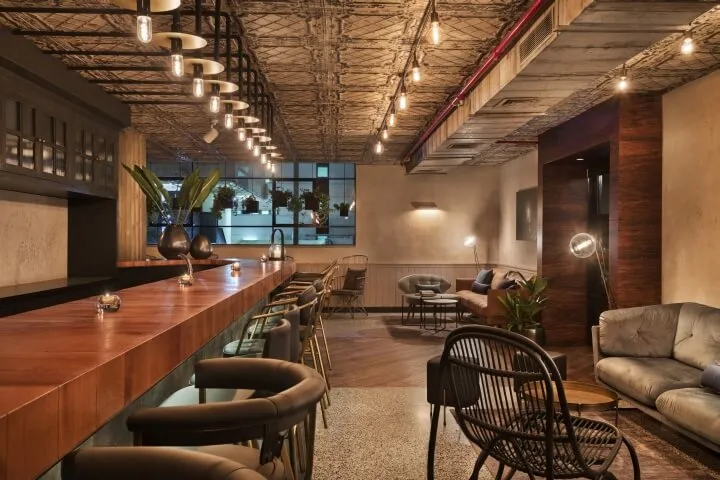 A modern bar interior featuring a wooden counter, contemporary lighting fixtures, and stylish seating arrangements.