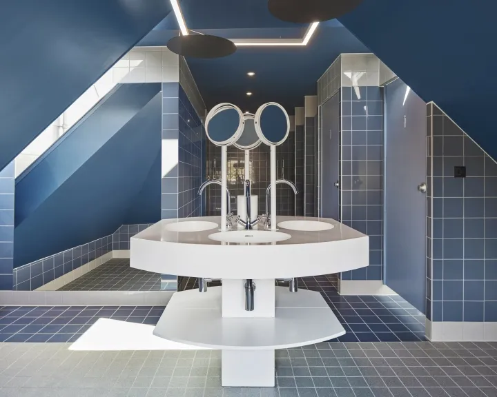 Modern public restroom with blue tiles, white sinks, and three circular mirrors.