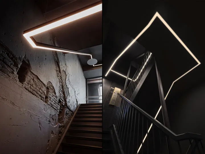 Modern, industrial-style staircase with black metal railing illuminated by linear, geometric lighting fixtures against a blac