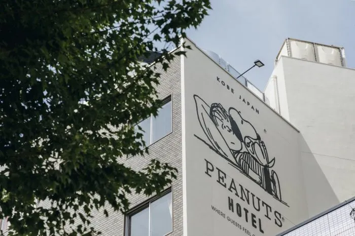 A hotel building exterior featuring brick and concrete materials, with a large mural of a Peanuts character on the side.