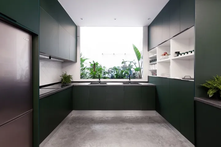Modern, spacious kitchen featuring dark green cabinetry and concrete countertops, with a large window revealing a lush green 