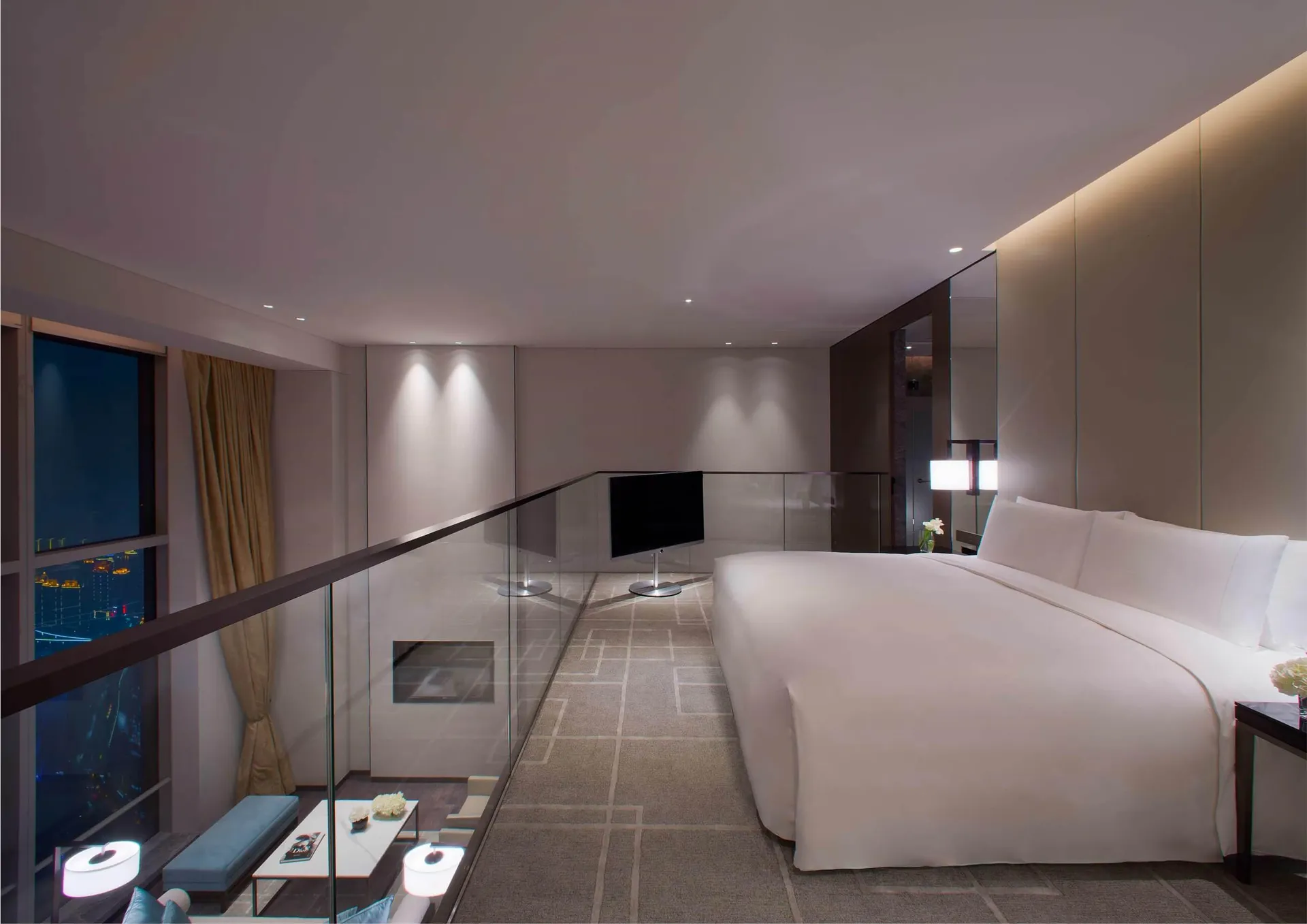 Modern minimalist bedroom with a white bed, glass railing, and floor-to-ceiling windows overlooking a cityscape.