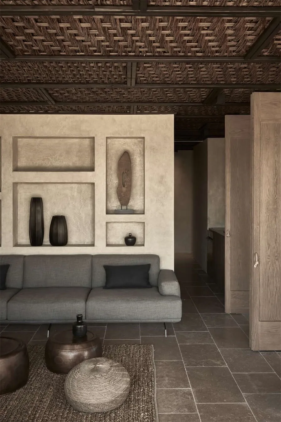 A modern living room with a concrete floor, minimalist furniture, and decorative wall niches filled with large vases.