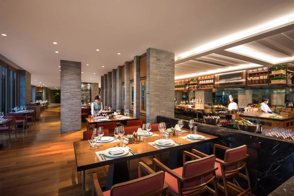 Modern restaurant interior with marble tables and chairs, stone flooring, and open kitchen counter.