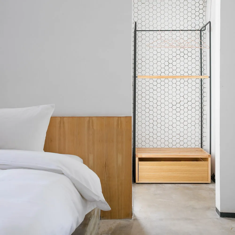 A minimalist bedroom with a white bed, wooden headboard, and modern storage system with an open grid design and built-in benc