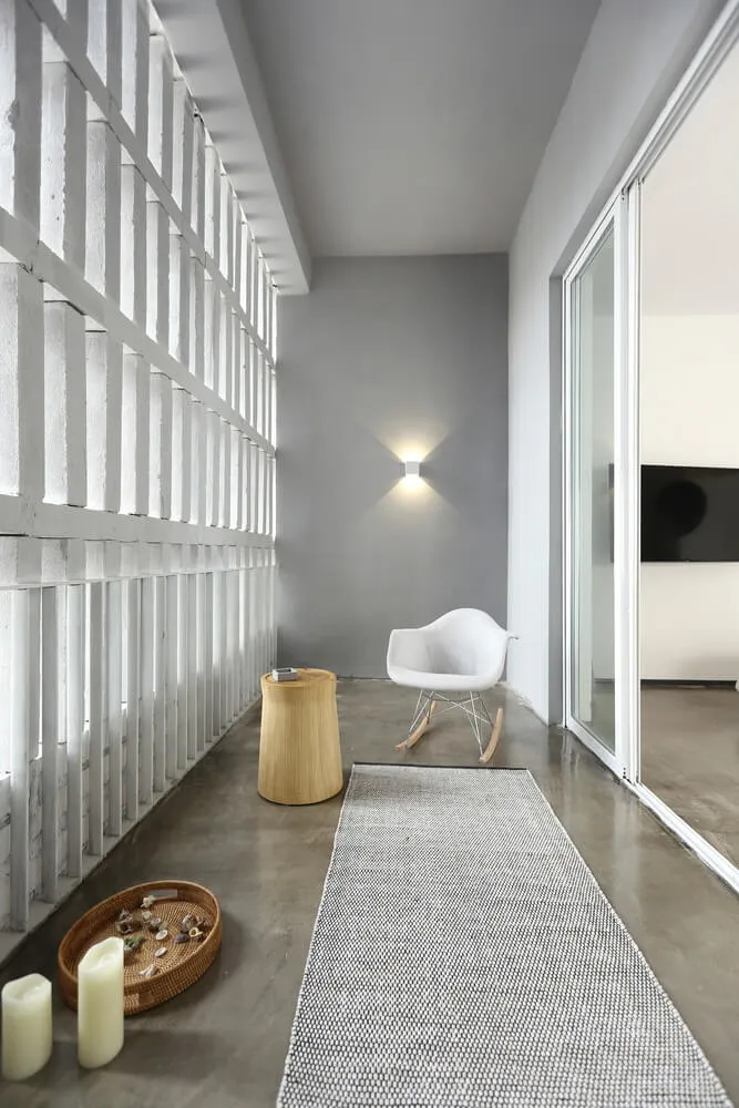 A minimalist living space featuring concrete walls and floor, with a white rocking chair, a wooden stool, and decorative item