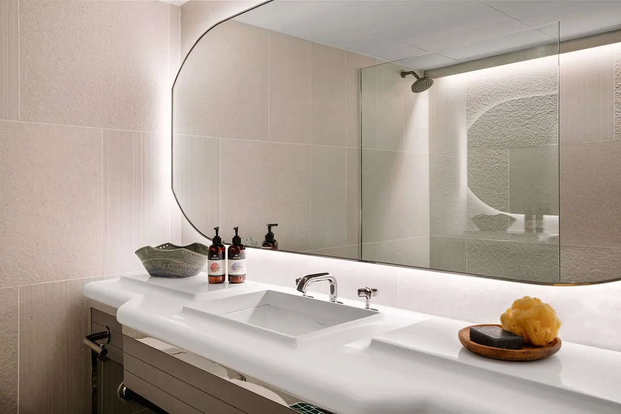A sleek, minimalist bathroom with a white ceramic sink, glass shower enclosure, and polished surfaces.