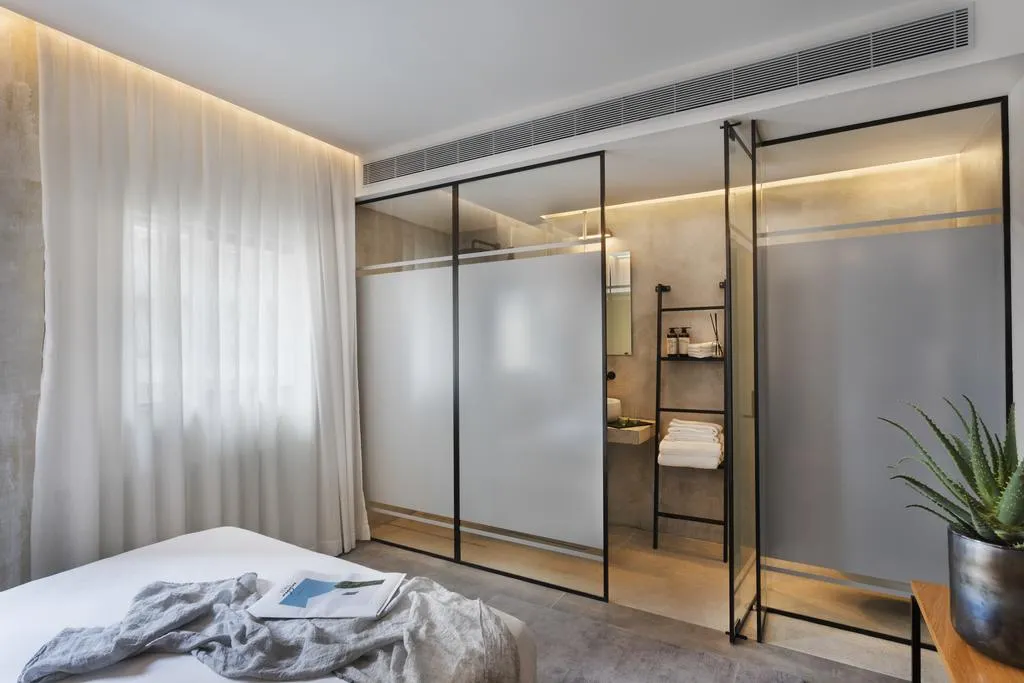 Modern minimalist bedroom with glass sliding doors, metal frames, and concrete floor.