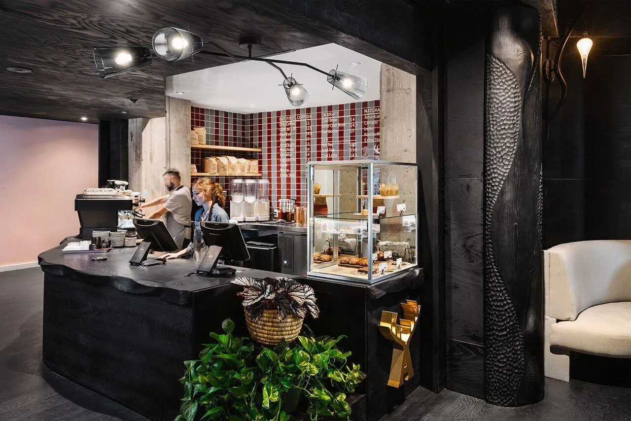 Industrial-style cafe interior with concrete wall, wooden counter, and green plants.