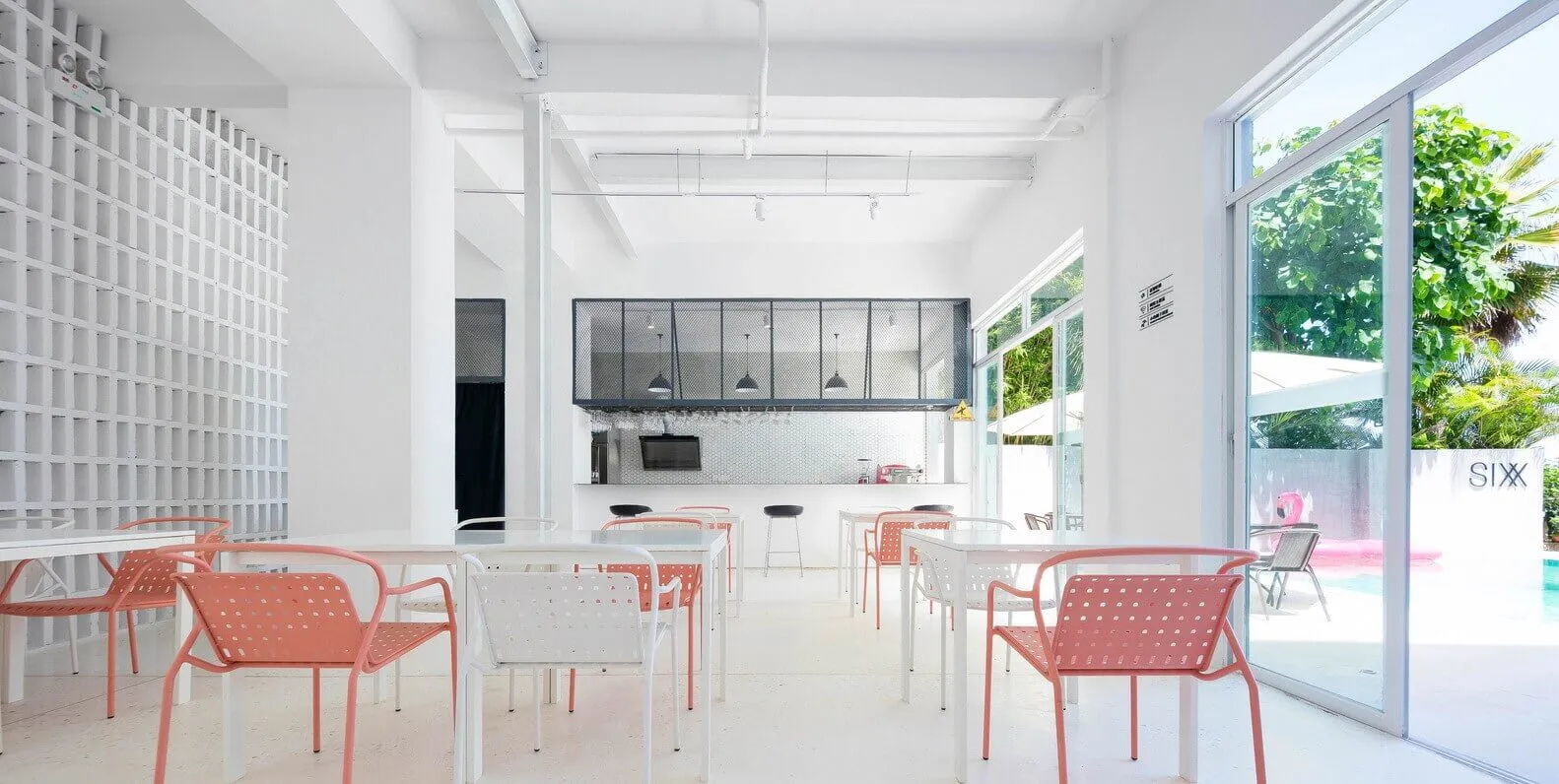 A minimalist cafe interior with white walls, pink chairs, and a bar counter