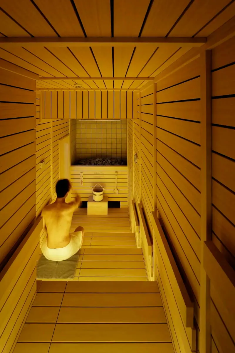 A minimalist sauna with wooden walls and a person sitting on a mat inside.