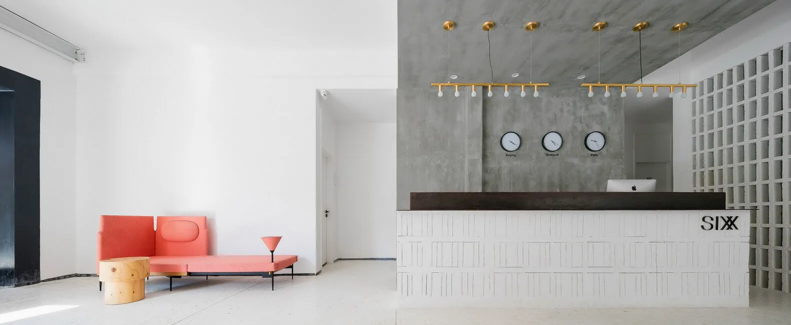 A modern lobby featuring a reception desk with clocks displaying time zones and a minimalist seating area with a pink couch a