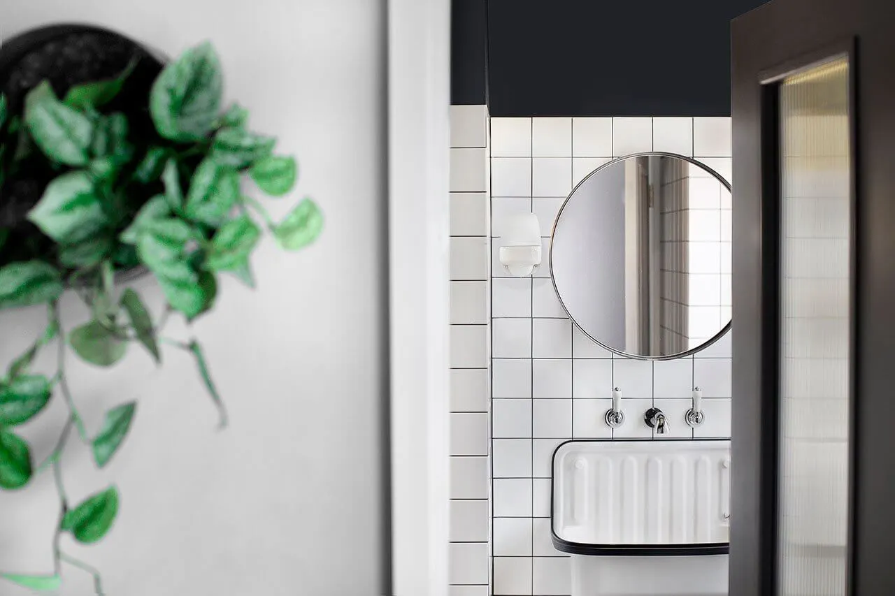A bathroom with a modern industrial design featuring white tiles, a round mirror, and a white sink.