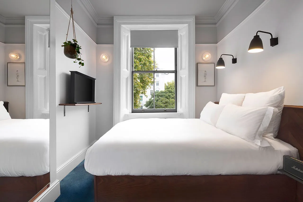 A minimalist bedroom featuring a white bed with a wooden headboard, white textiles, and minimalist decor.
