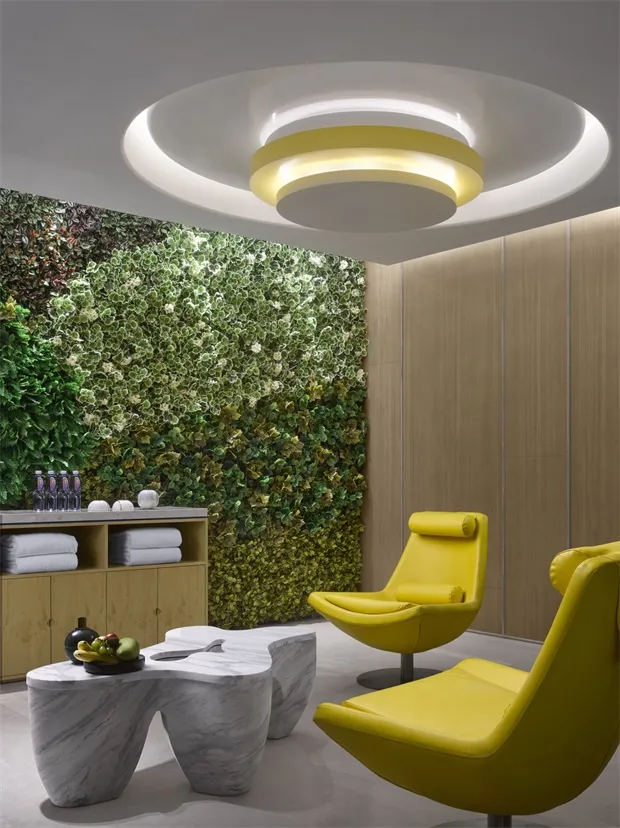 A modern living space featuring a vertical garden, marble table, yellow chairs, and wooden walls.