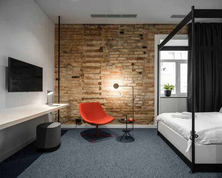 A minimalist bedroom featuring a red chair, a modern bed, and a brick wall.