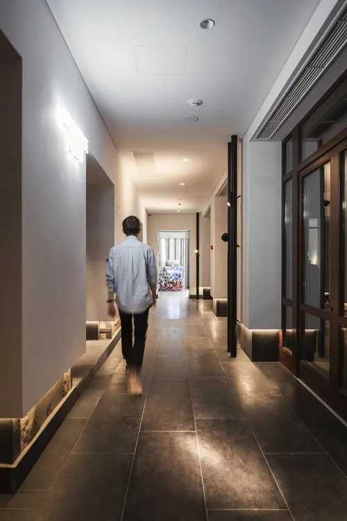 A minimalist corridor adorned with concrete tiles, featuring a lone individual walking away from the camera.