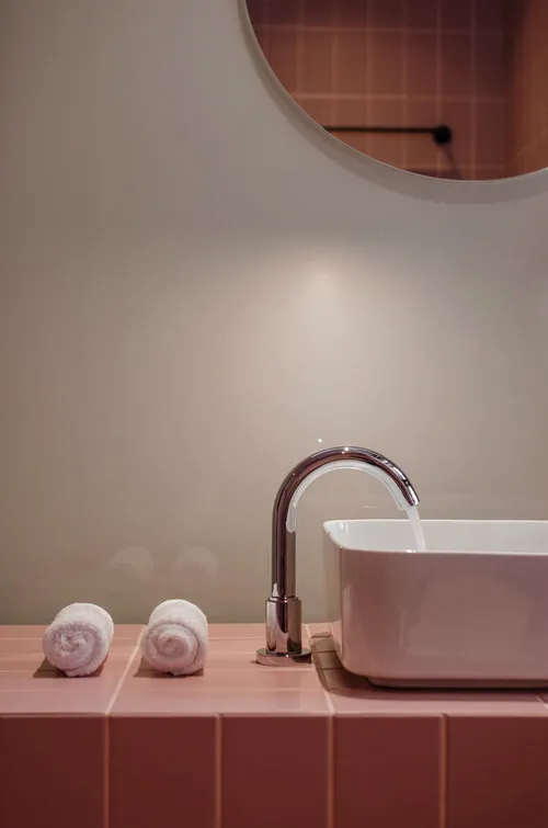 Modern bathroom with a sink, faucet, and three white towels on a pink tiled countertop.
