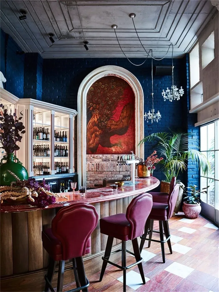 An industrial-themed bar with a marble counter, purple stools, and a large mural of a rooster on a red background.