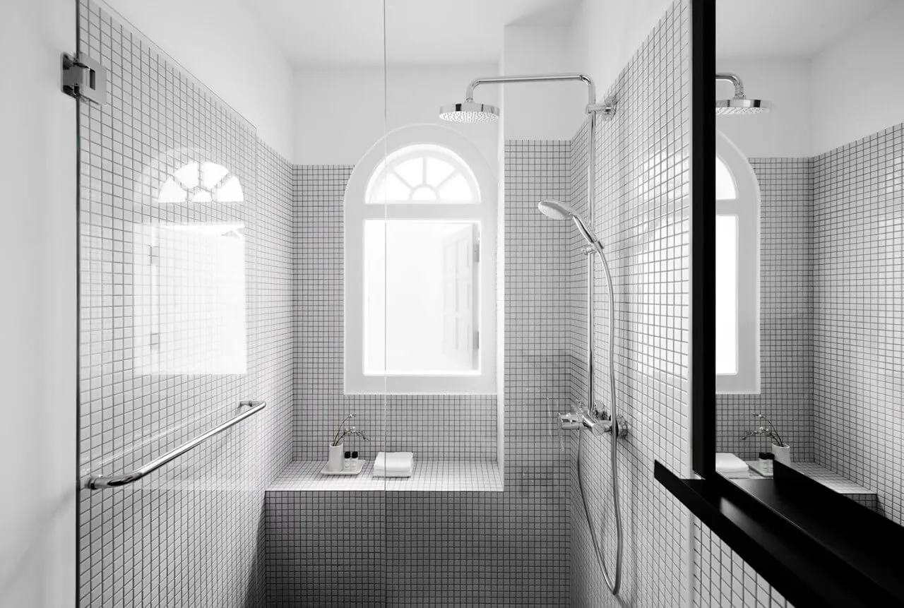 Modern bathroom with white tiled walls, glass shower enclosure, and arched windows.