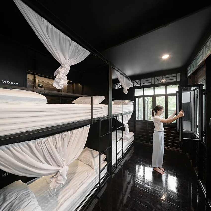 A modern bedroom with a black interior, featuring twin beds dressed in white textiles with fabric curtains for privacy.