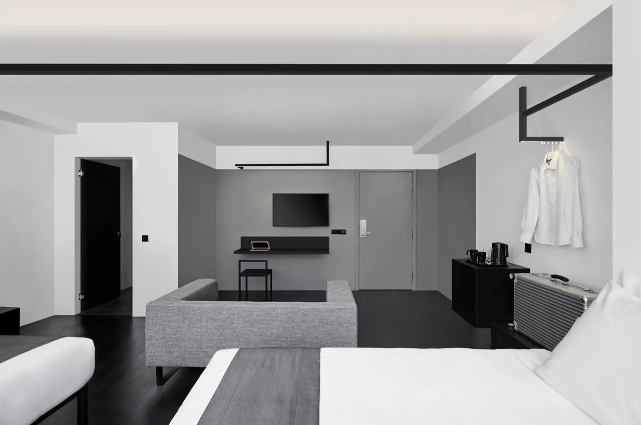 Modern minimalist hotel room featuring a concrete floor and furniture, with a television mounted on the wall and a stylish wh