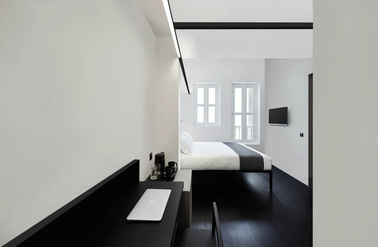 Modern minimalist bedroom featuring a metal-framed bed, wooden flooring, and fabric bedding.