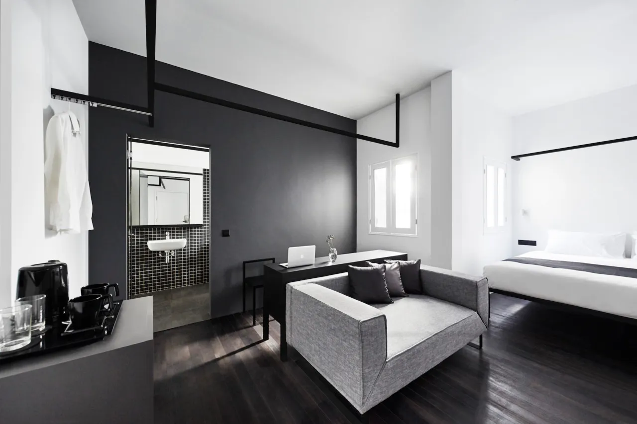A modern minimalist bedroom with black, white, and gray tones featuring a simple sofa, a bed with a black and white comforter