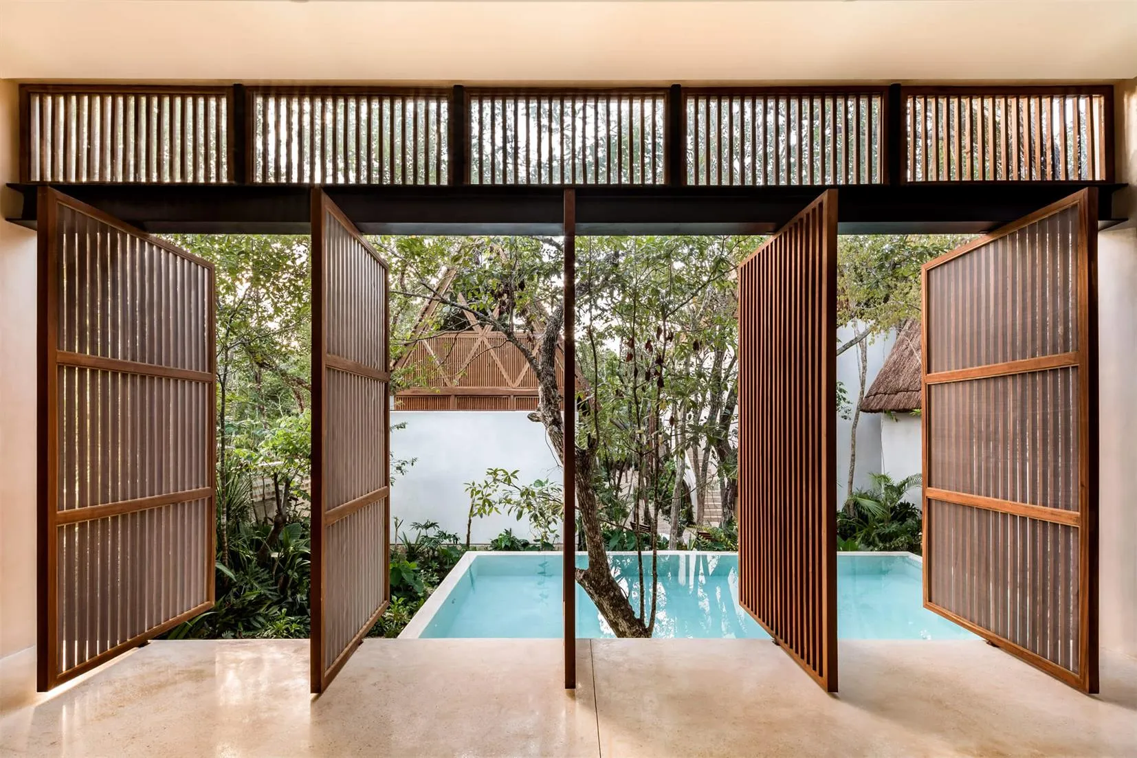 An open wooden gate, revealing a serene pool and lush greenery.
