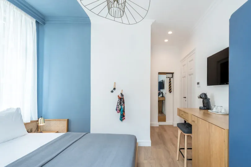 Minimalist bedroom with blue walls, a grey double bed, and a wooden desk with a coffee maker.