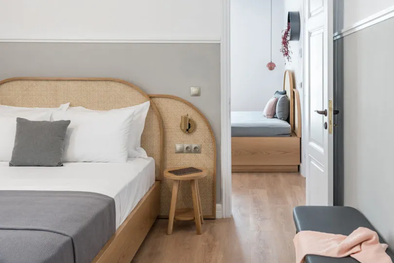 A minimalist bedroom featuring a wooden frame bed with white bedding and a wooden stool.