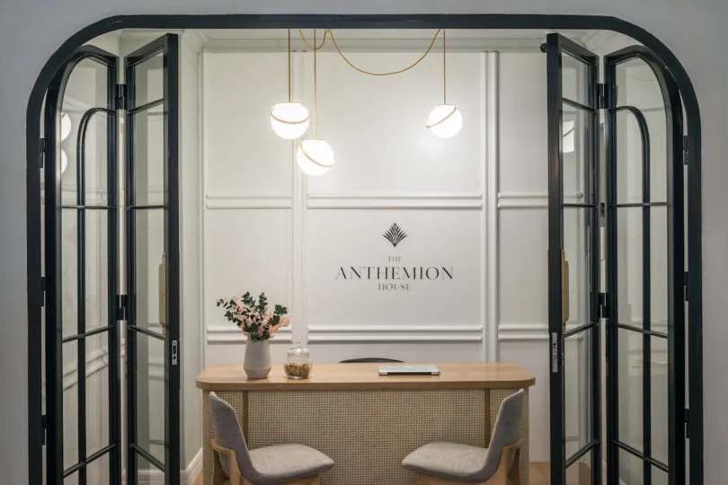 Modern minimalist office reception area with glass and wooden surfaces, potted plant, and hanging lights.