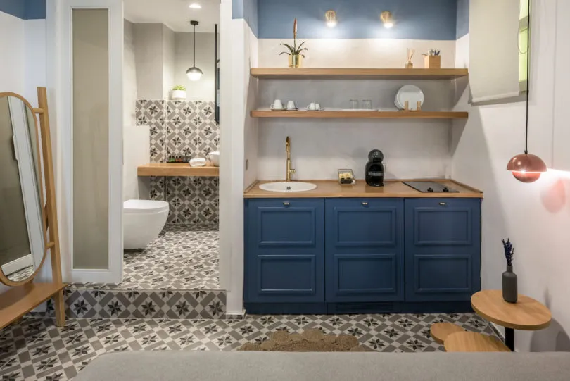 A modern kitchen with blue cabinets and white surfaces, featuring a wooden countertop and a patterned floor.