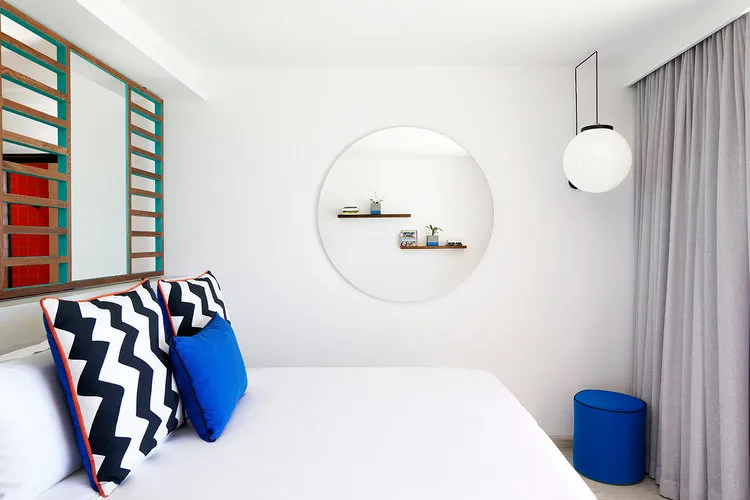 Minimalist bedroom with white walls, blue and black geometric pillows on a bed, and a hanging globe light fixture.