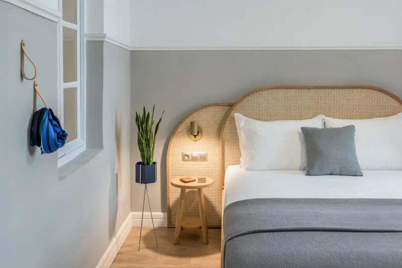 Modern, minimalist bedroom with a cozy woven rattan headboard, white bedding, and a small wooden bedside table.