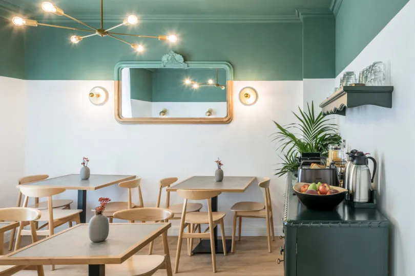 A cozy breakfast cafe with wooden tables, green paint walls, and a modern chandelier.