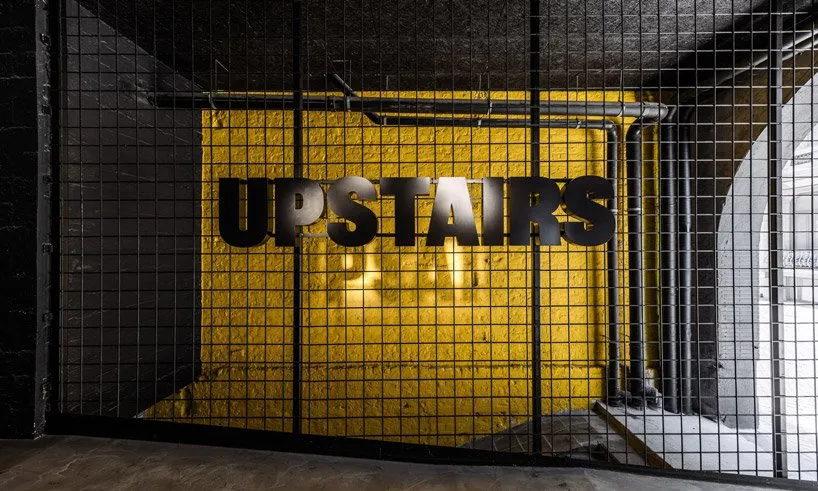 Industrial sign that says 'UPSTAIRS' mounted on yellow tiled wall in an industrial-style interior