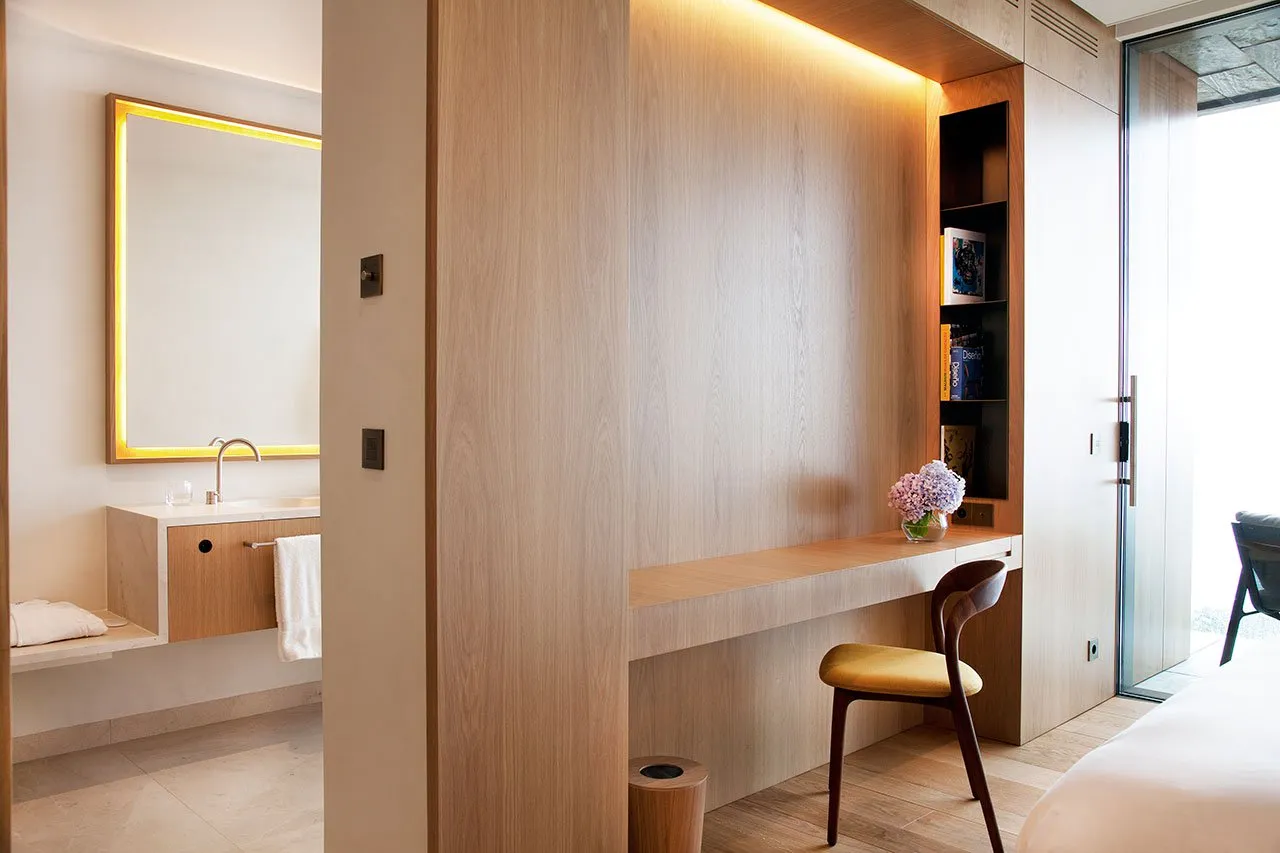 A minimalist hotel room featuring a wooden wall desk with a vases and books.