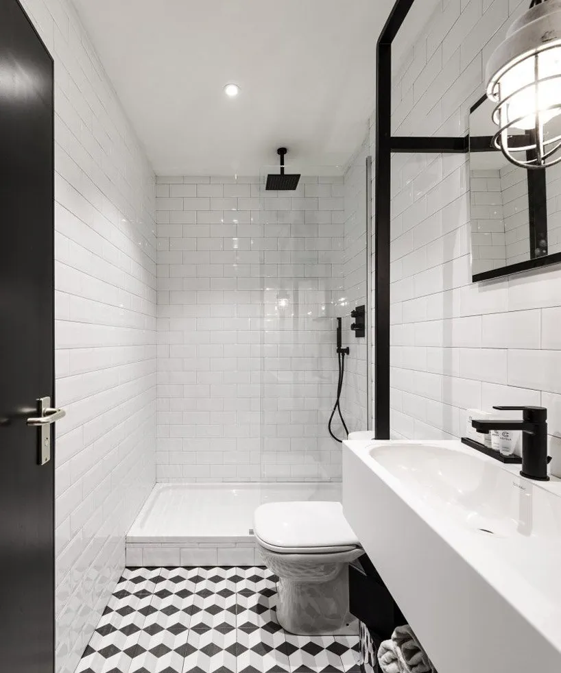 A modern bathroom featuring white subway tiles, a black toilet, and a black and white geometric floor tile pattern.