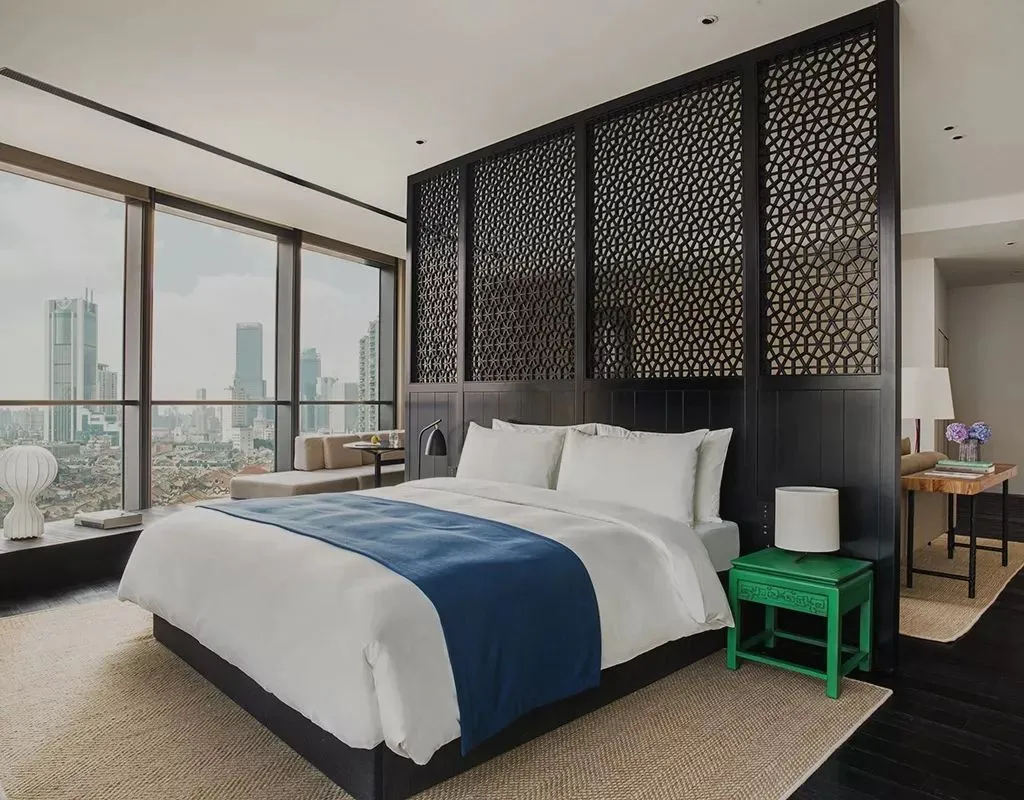 Modern bedroom featuring a glass wall, black headboard, and mixed materials, showcasing contemporary design and comfort.
