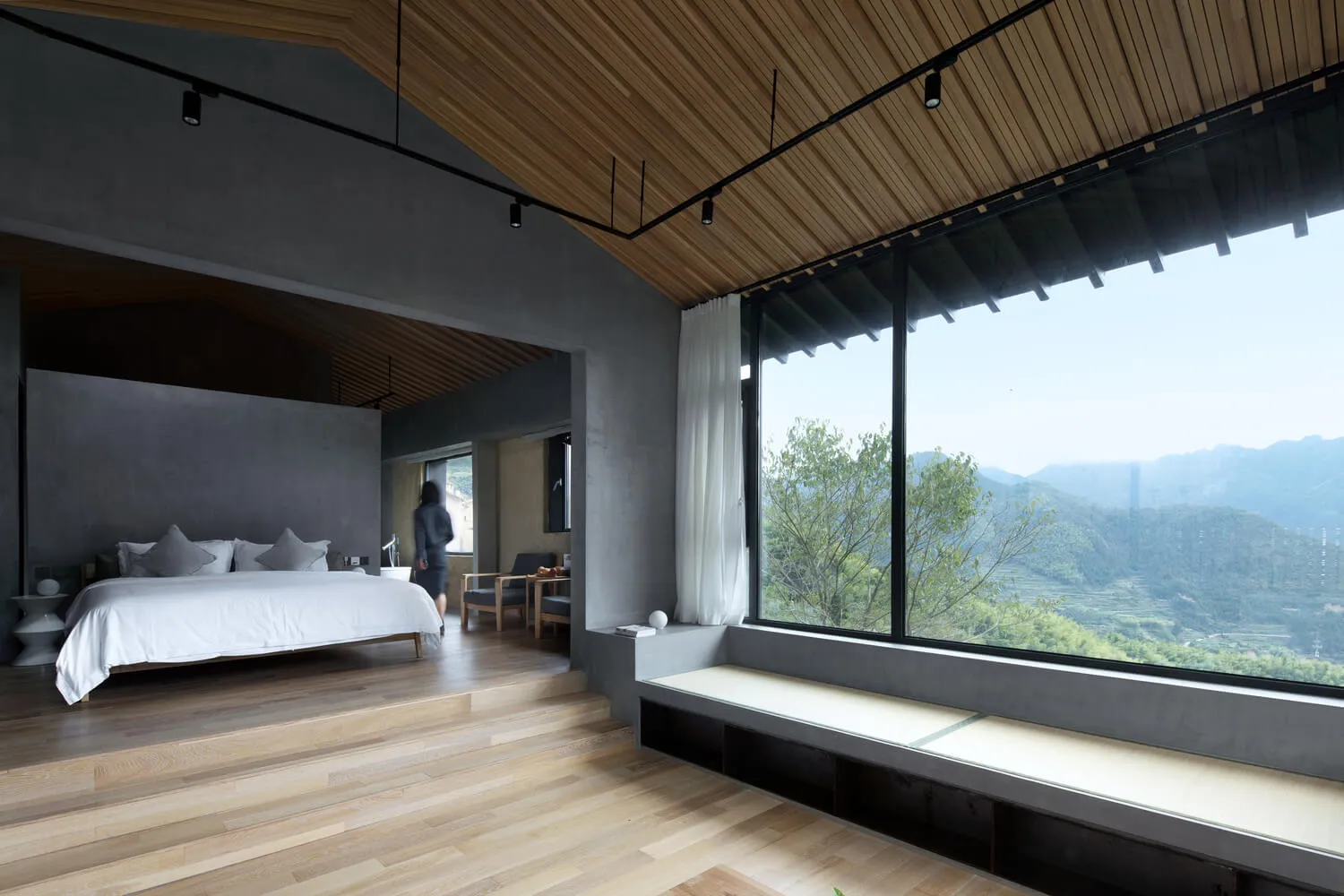 A modern living room featuring a wooden floor, large windows, a minimalist design, and a view of mountains and trees.
