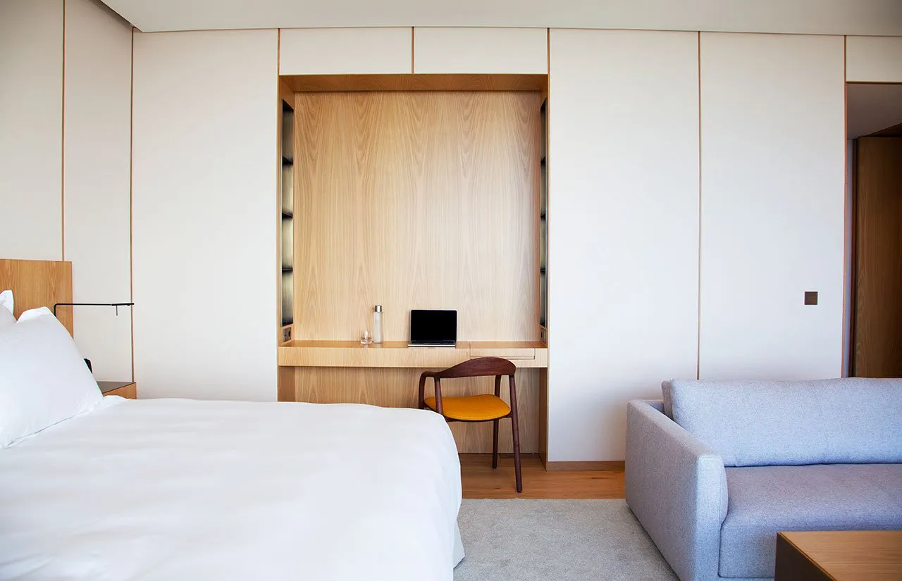 Modern minimalist bedroom featuring a wooden desk and white fabric furniture.