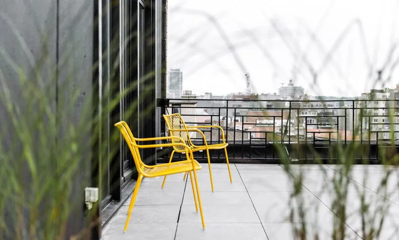 Outdoor patio scene with modern, yellow metal chairs against a cityscape.